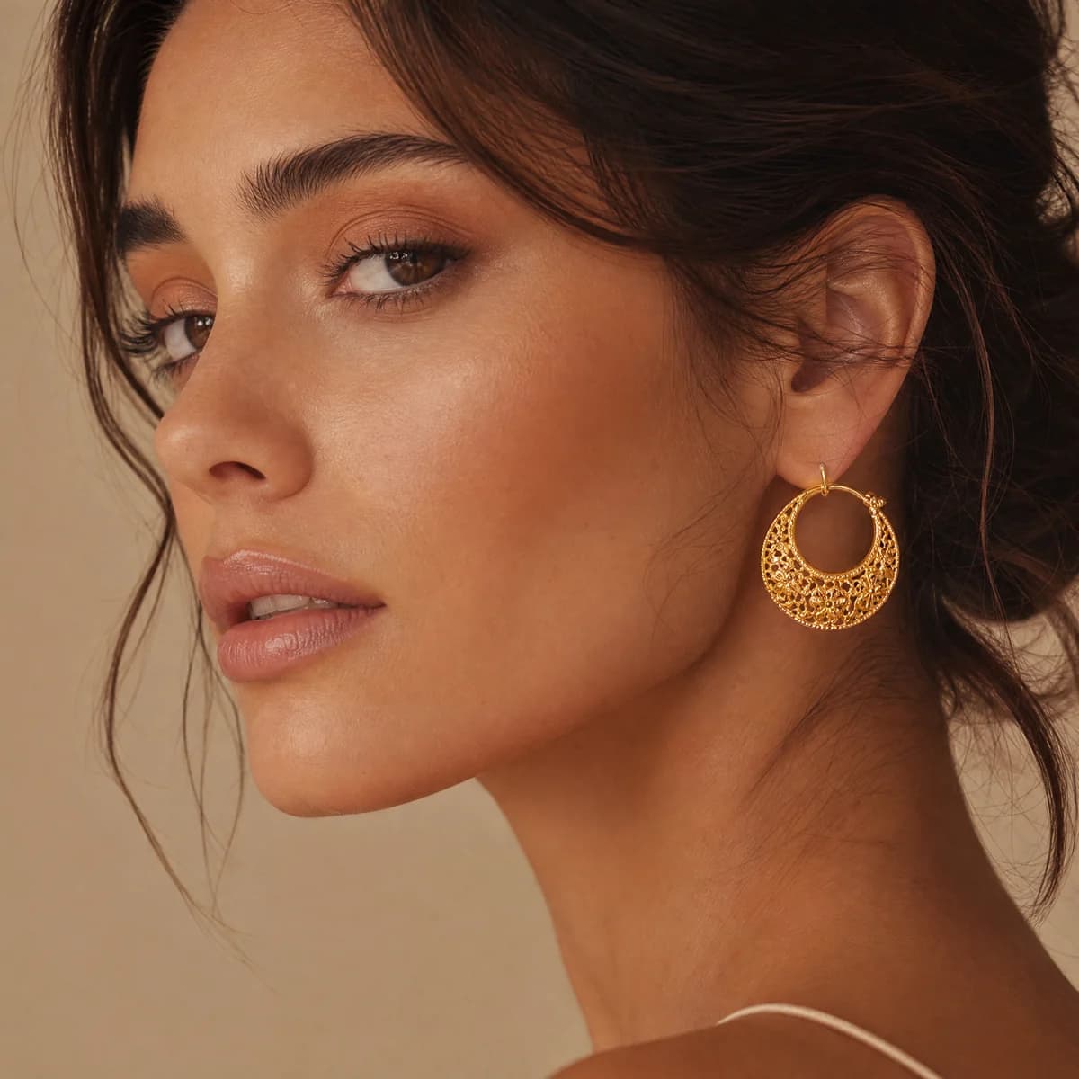 Close-up of a woman wearing a circular gold earring with a decorative openwork pattern