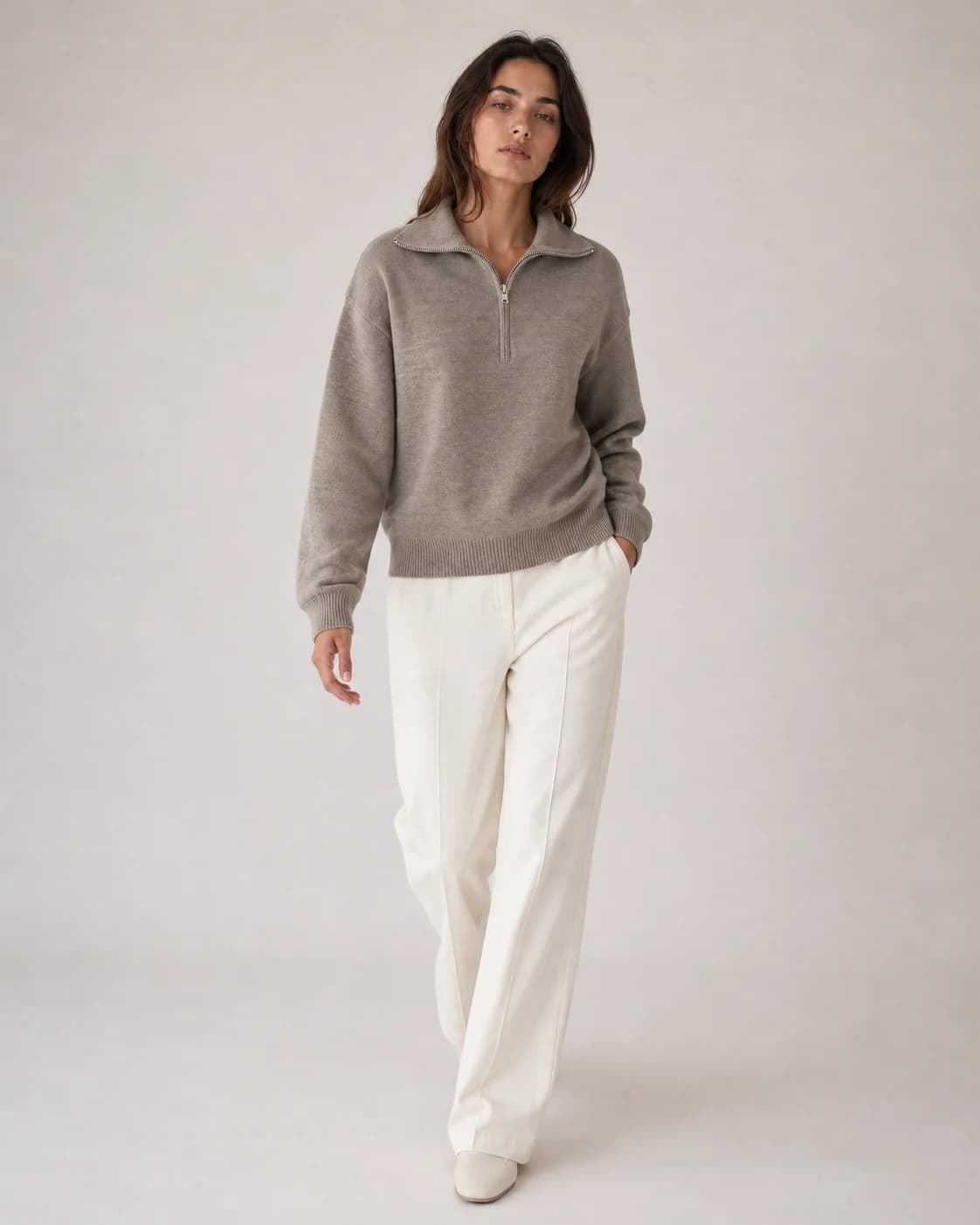 Full-length view of a woman wearing a grey half-zip pullover and white trousers