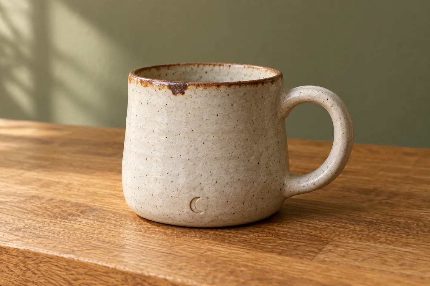 Synthetic reference: speckled ivory mug with a brown rim and crescent mark on an oak counter