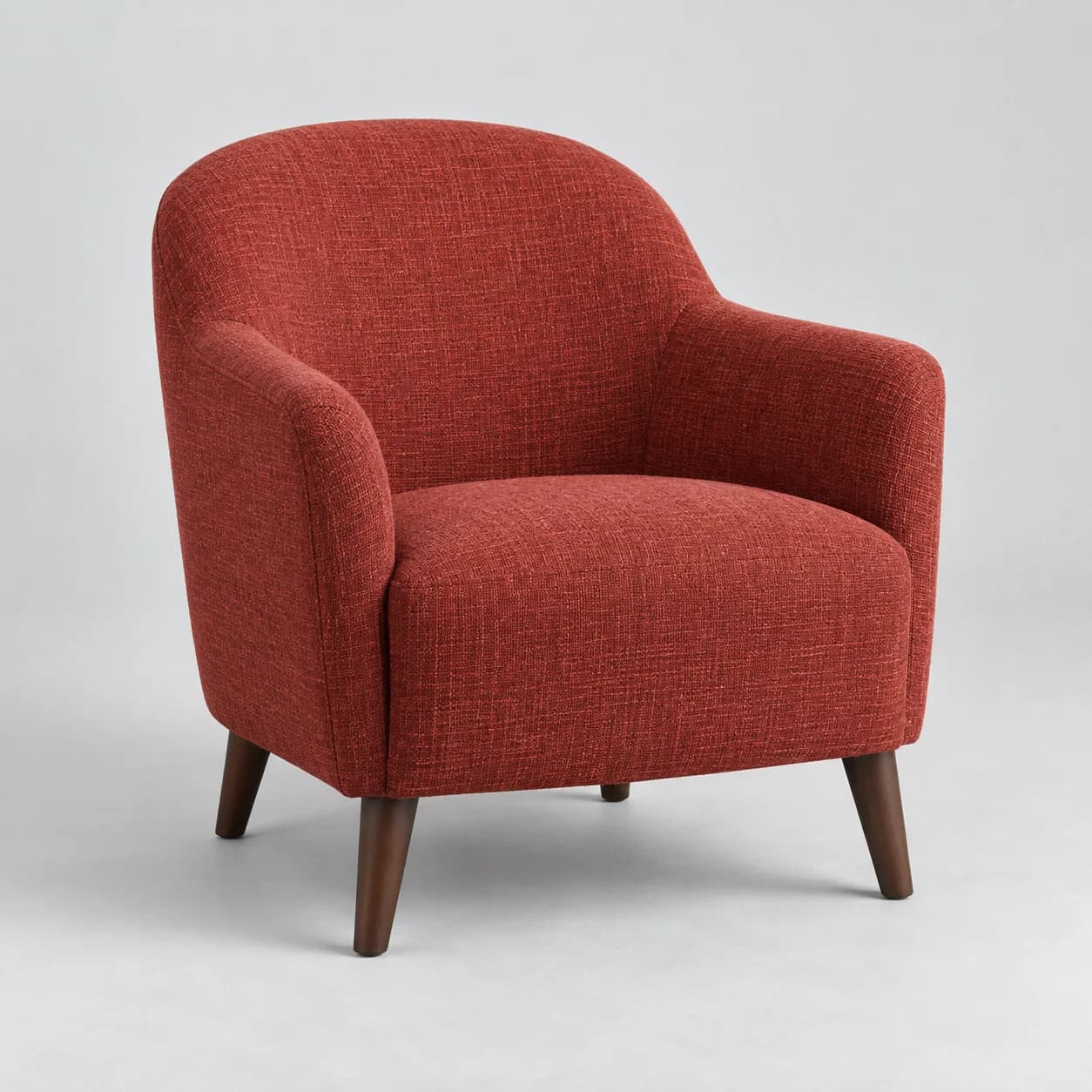 Small brick-red upholstered chair with dark wooden legs on a studio backdrop